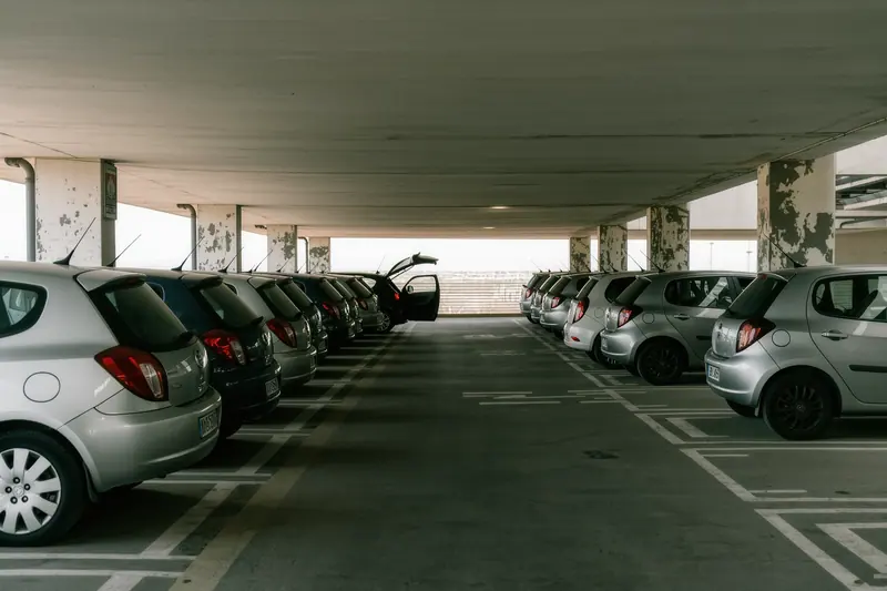 A rental car pickup deck in an airport car park, rows of unbranded hatchbacks in numbered bays, one boot standing open.