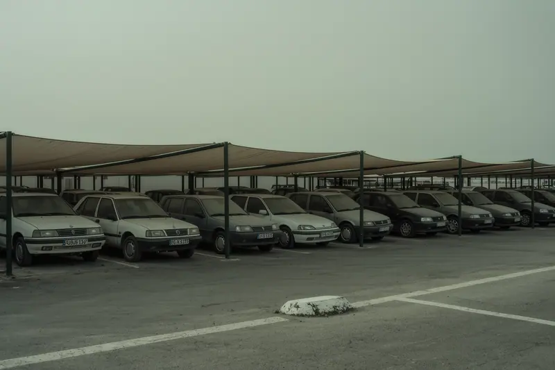 A quiet long-stay parking lot with dusty cars standing under thin shade sails on the Costa del Sol.