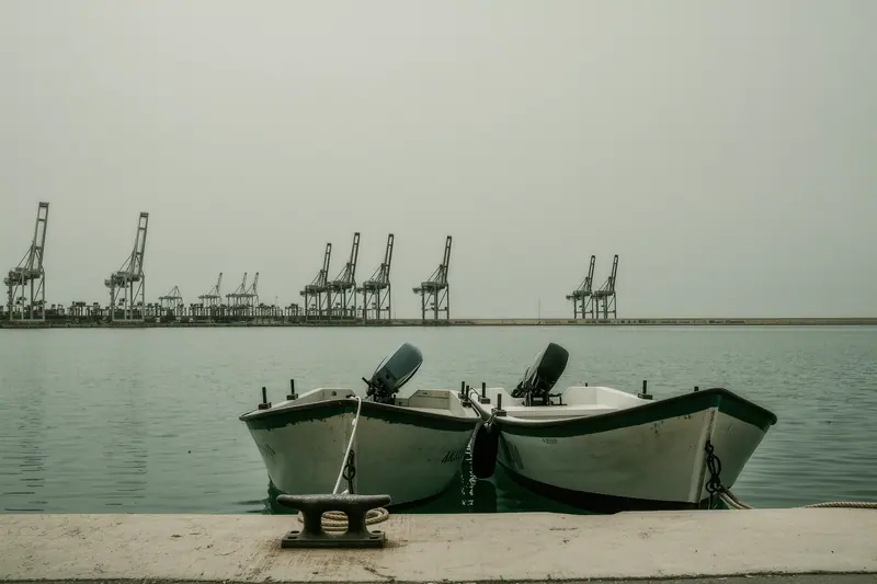 Small motorboats tied bow-to at a floating pontoon in Málaga port, harbour cranes and a breakwater behind them.