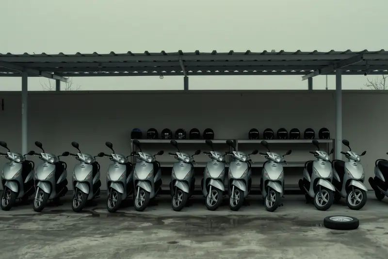 A line of rental motorbikes with plain fairings parked nose-in under a canopy, helmets on a shelf on the wall behind them.