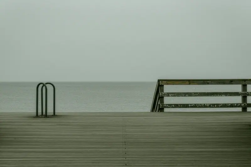 An empty boardwalk section of the coastal path behind a beach, with a bike rack and a wooden handrail, flat grey sea beyond.